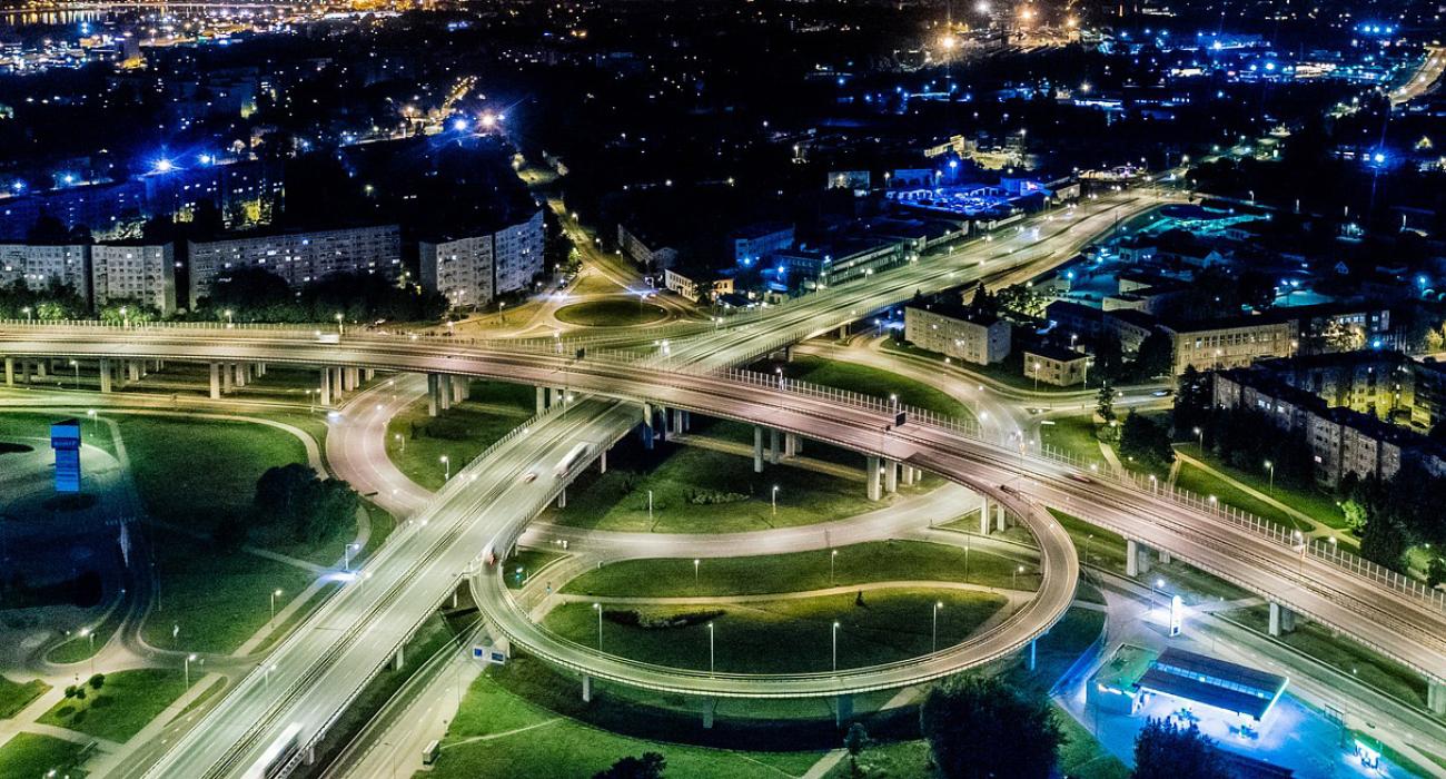 A stack interchange over a green park area with city buildings surrounding it