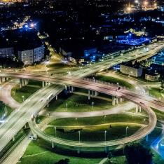 A stack interchange over a green park area with city buildings surrounding it