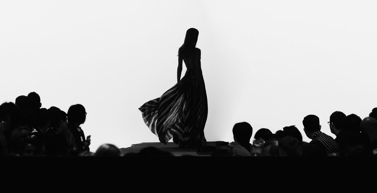 Silhouette of a fashion model on a runway with large audience