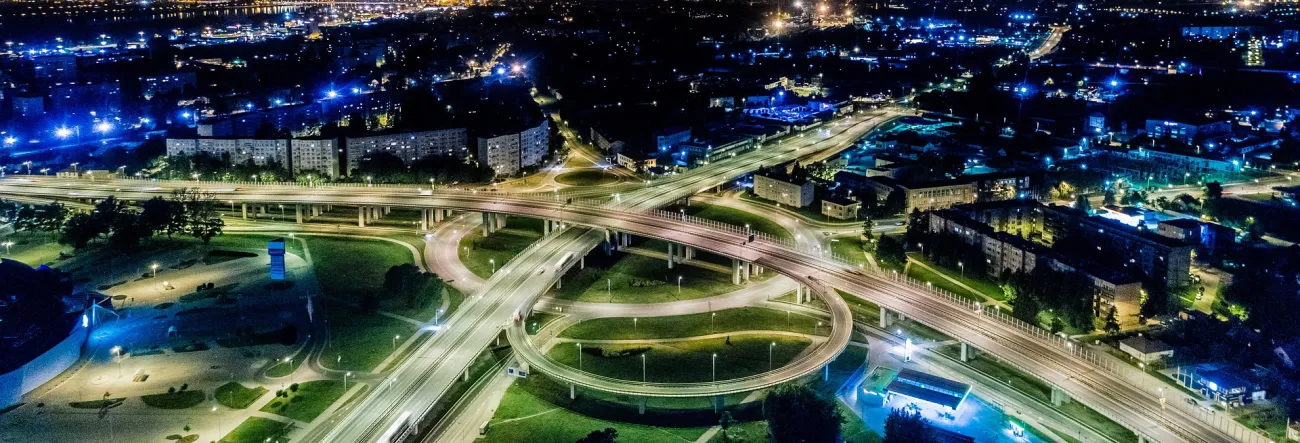 A stack interchange over a green park area with city buildings surrounding it